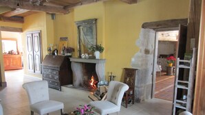 A cozy living room with a fireplace, white chairs, a wooden coffee table with a plant, and a bookshelf. - Le Relais des Deux Tours (Bremondans)