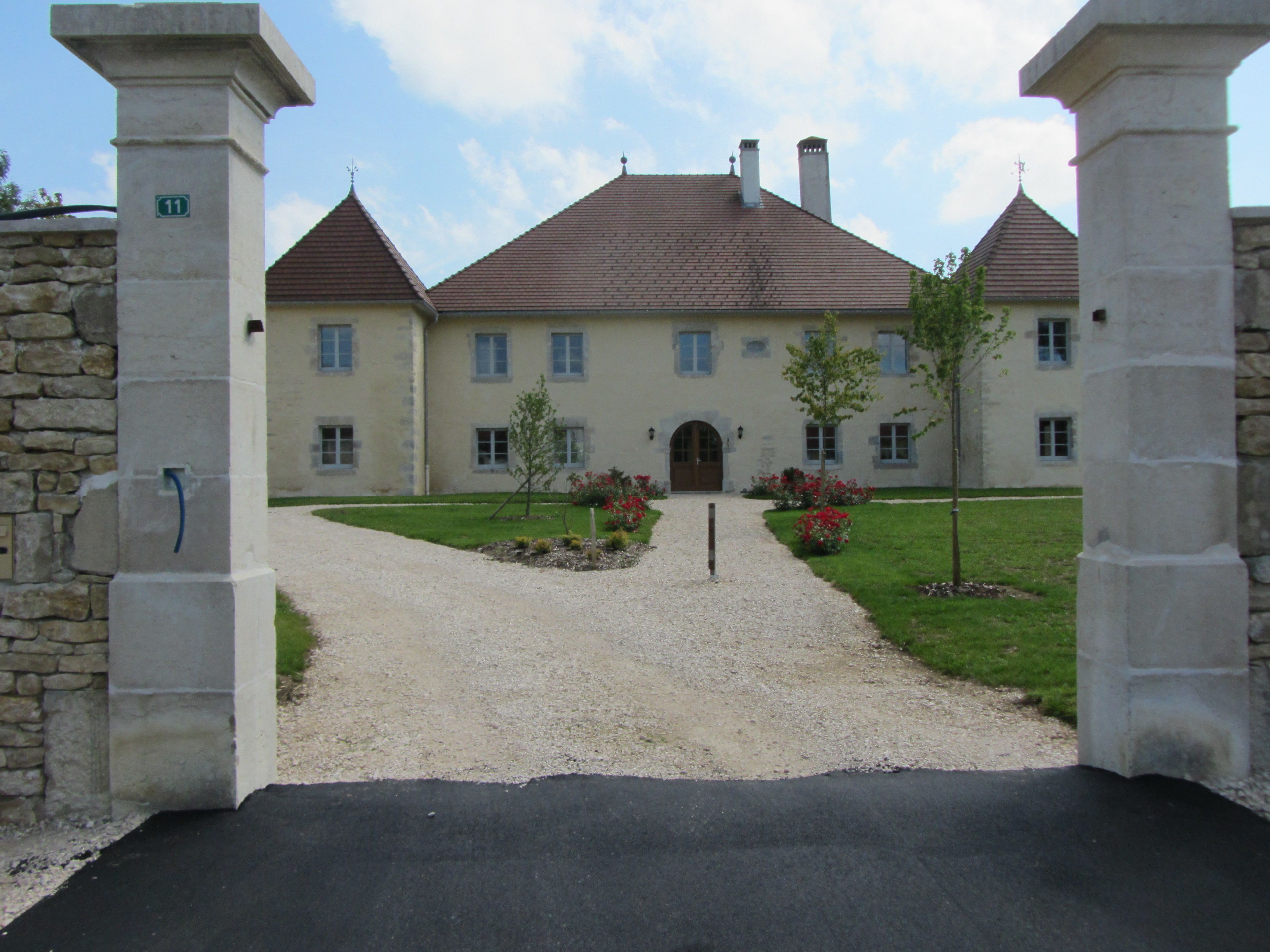 A large, two-story building with a symmetrical facade, a gravel driveway leading to a blacktiled entrance, and a well-maintained lawn with red flowers.