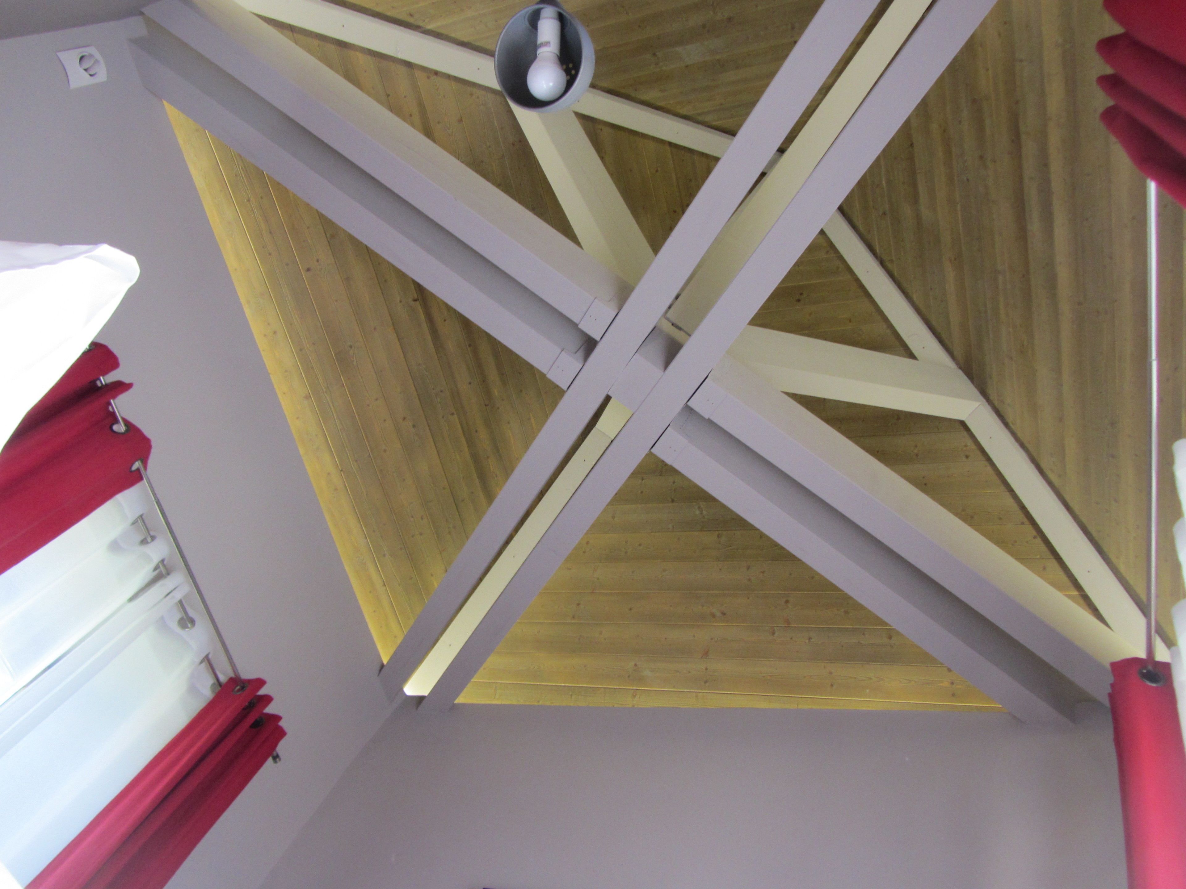 Una habitación con techo inclinado, vigas de madera y una lámpara.