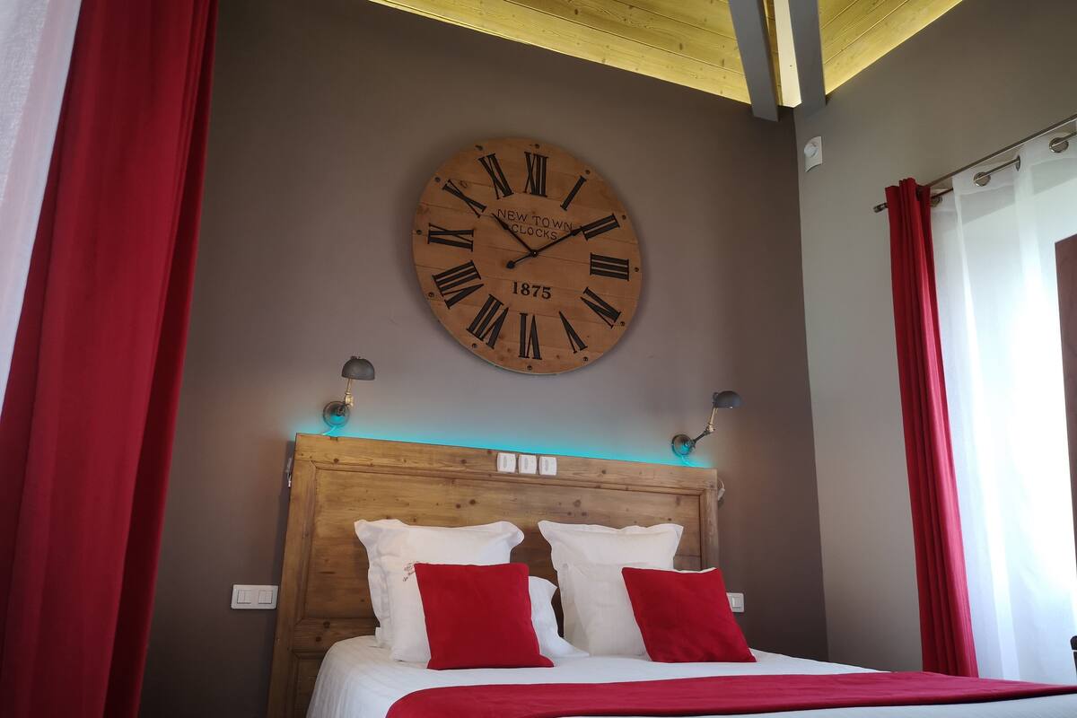 Quarto com cabeceira de madeira, um relógio de parede grande e cortinas vermelhas.