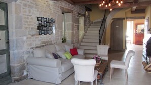A spacious living area with a stone wall, a staircase, and a cozy seating arrangement. - Le Relais des Deux Tours (Bremondans)