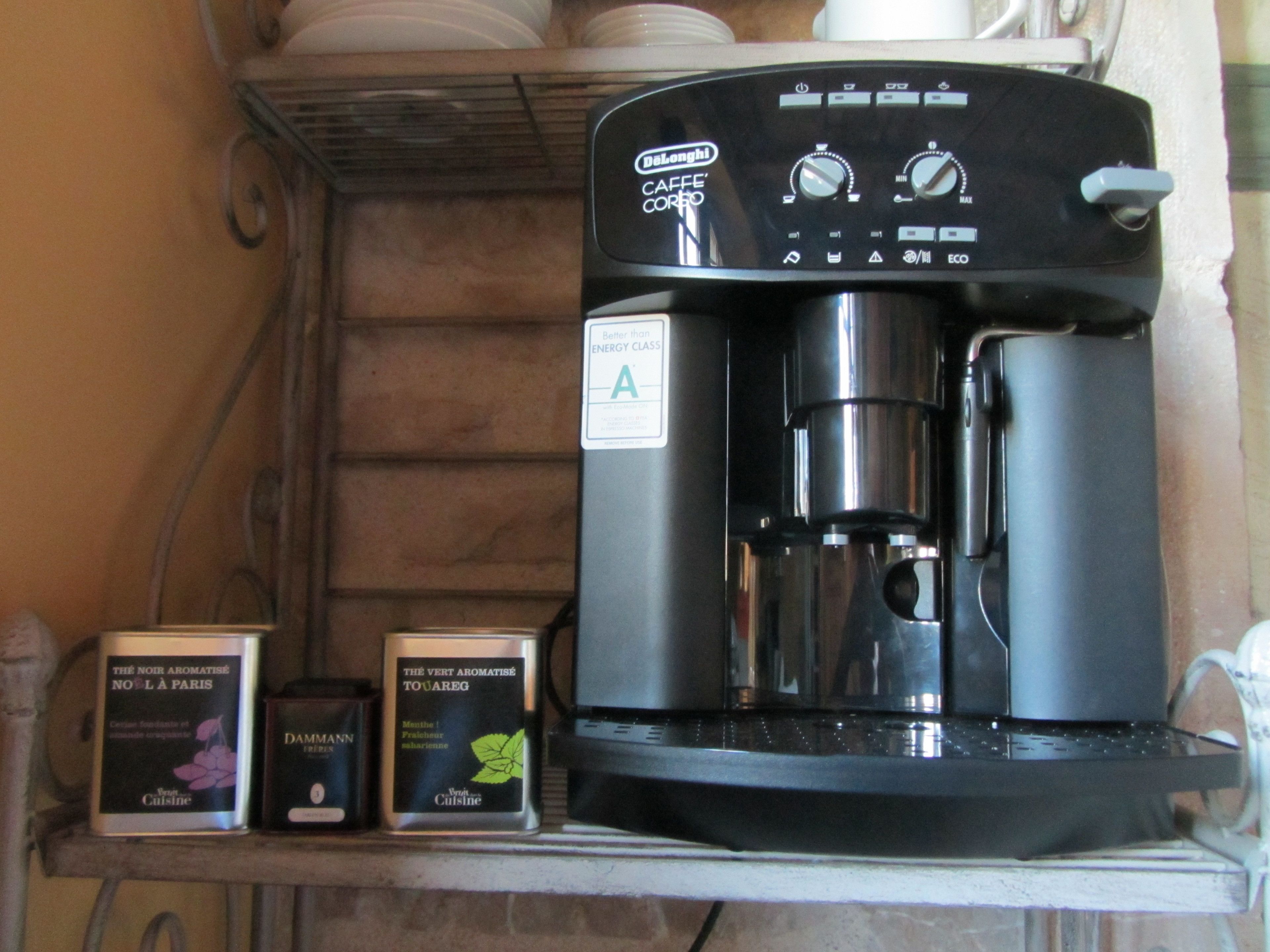 Una cafetera con un panel de control, dos cápsulas de café y una taza blanca sobre una repisa.