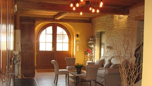A cozy room with a wooden ceiling, two large arched windows, a sofa, a dining table with chairs, and a decorative vase. - Le Relais des Deux Tours (Bremondans)