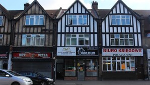 A row of traditional timber-framed buildings with shops on the ground floor, including a pizza restaurant and a vision estate office. - Guest House London (London)