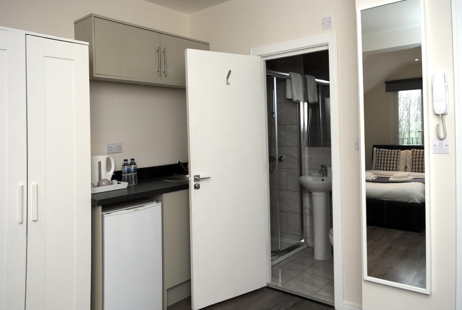 Une chambre d’hôtel de taille réduite, dotée d’une kitchenette, d’une douche et d’un lit.