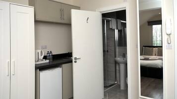 Une chambre d’hôtel de taille réduite, dotée d’une kitchenette, d’une douche et d’un lit.