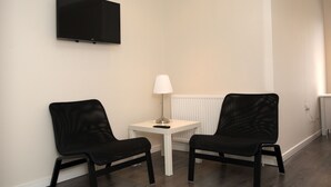 A room with two black chairs, a white table, a lamp, and a mounted TV on the wall. - Guest House London (London)