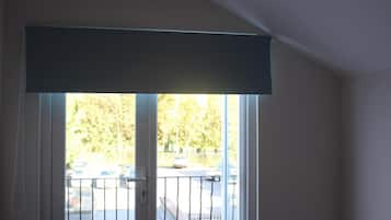 A room with a large window, a door with a white frame, and a view of parked cars and trees outside.