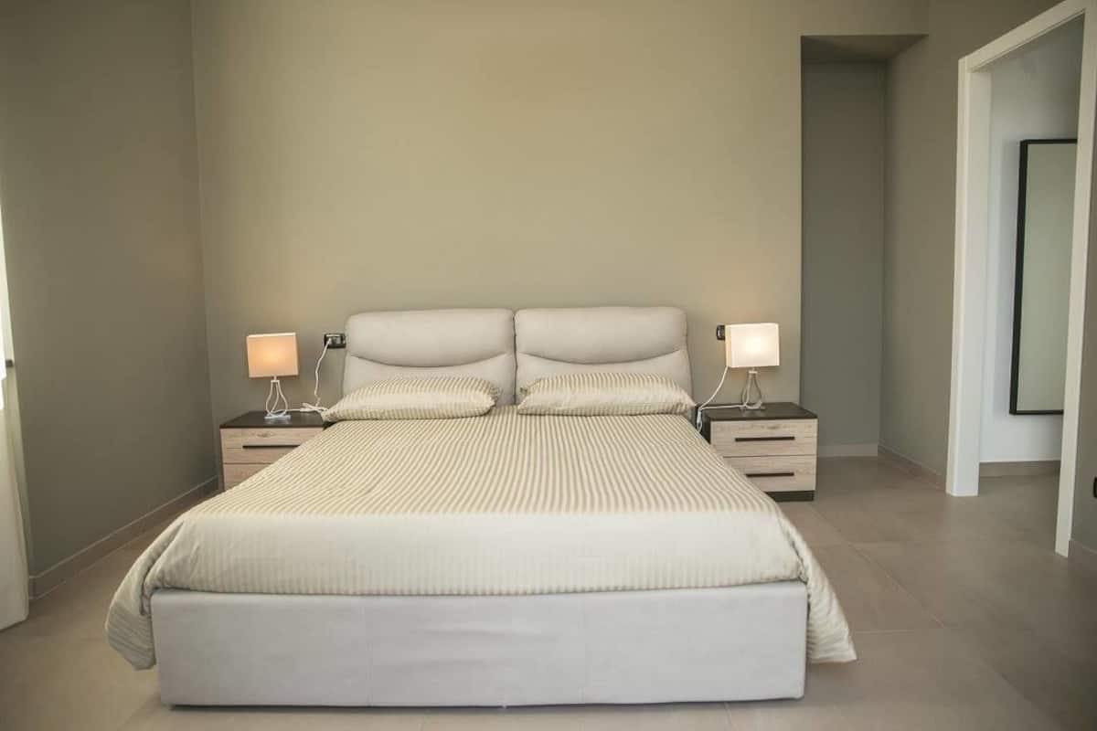 A modern bedroom with a large bed, two bedside tables, and two wall-mounted lamps.