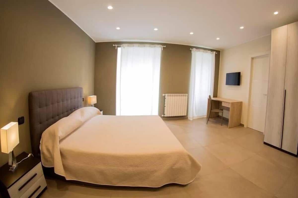 A bedroom with a large bed, bedside lamps, a desk, and a TV.