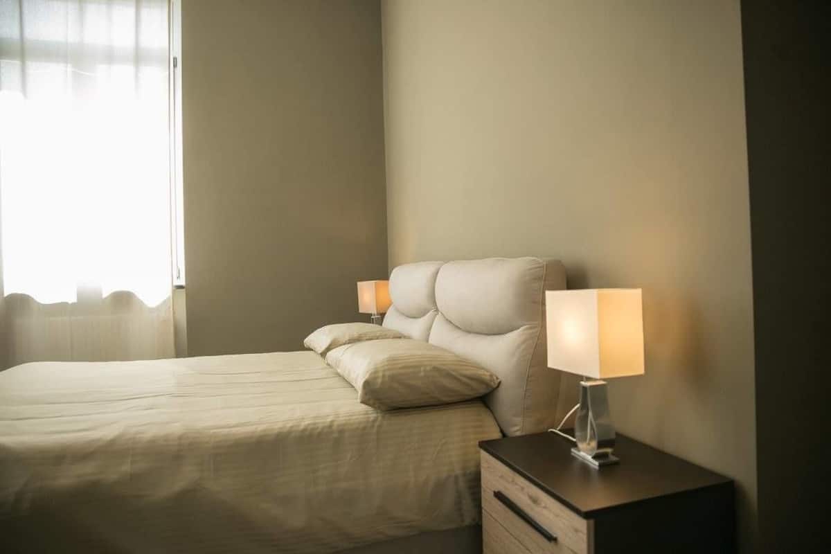A neatly made bed with two pillows and a bedside table with a lamp.