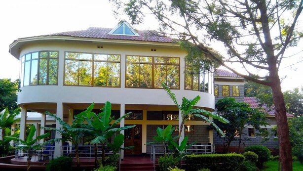 A two-story building with a curved facade, large windows, and a central entrance with steps. - Green Hills Lodge (Karatu)