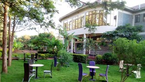 A courtyard with outdoor seating, surrounded by lush greenery and a building with large windows. - Green Hills Lodge (Karatu)