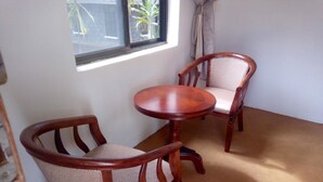 A room with two wooden chairs and a small round table, carpeted floor, and a window with a view of greenery. - Green Hills Lodge (Karatu)