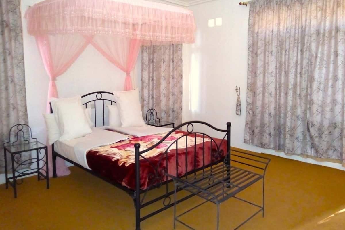 A single bed with a metal frame, a bedside table, and a canopy bedspread.