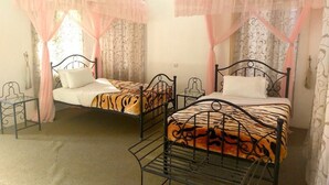 Two twin beds with mosquito netting, a small table, and patterned curtains in a room. - Green Hills Lodge (Karatu)