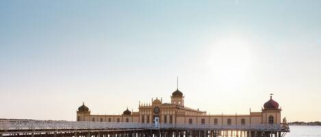 A large, multi-domed building with a prominent clock tower, connected to the shore by a pier.