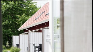 A wooden deck with a table and chairs, a covered outdoor seating area, and a view of a red-roofed building. - Apelviken Lägenhetshotell (Varberg)