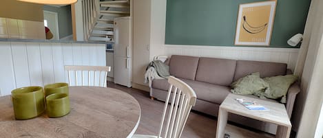 A compact living space with a dining table, a sofa, a small side table, and a kitchen area with a staircase.