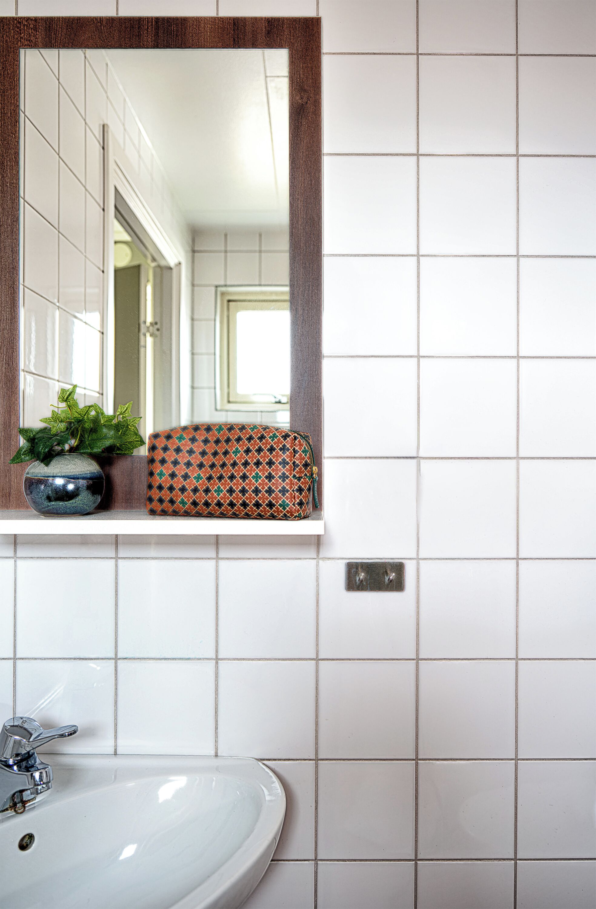 A bathroom with a white sink, a mirror with a wooden frame, and a patterned box on the countertop.
