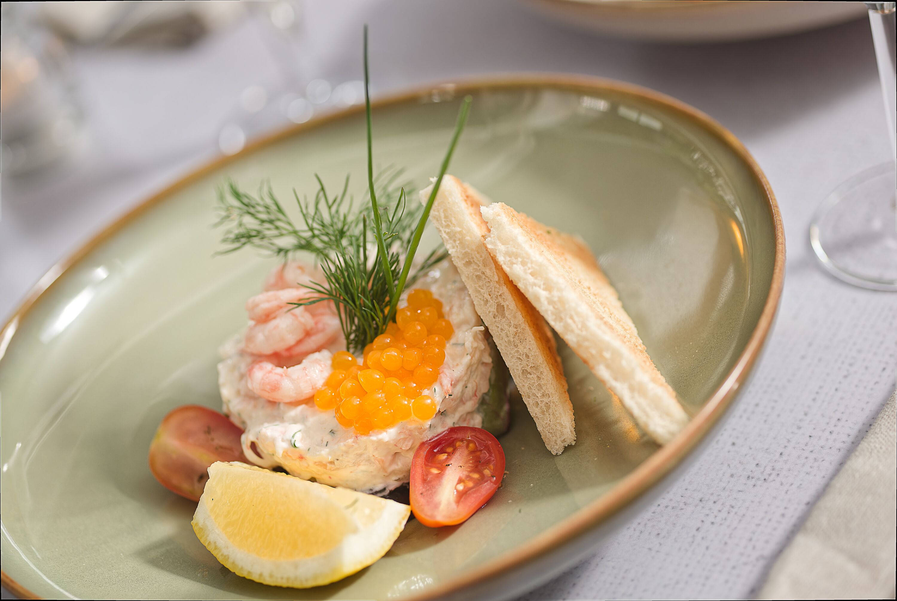 Une assiette contenant des crevettes, du caviar, une tranche de citron, une tomate et une branche d’aneth.