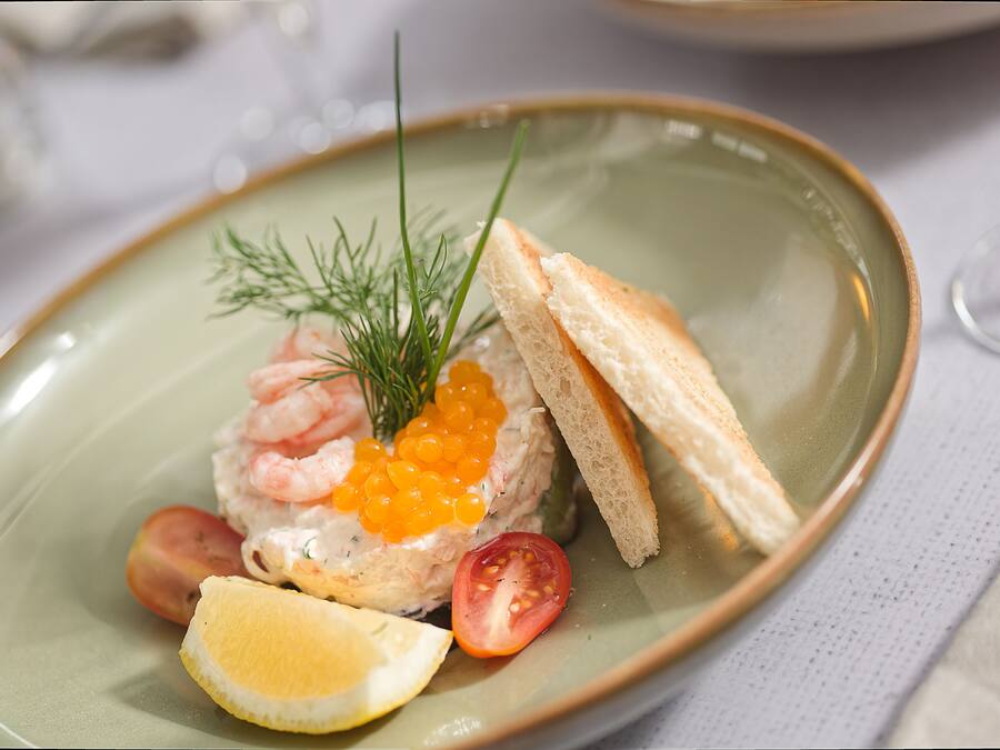 Une assiette contenant des crevettes, du caviar, une tranche de citron, une tomate et une branche d’aneth.