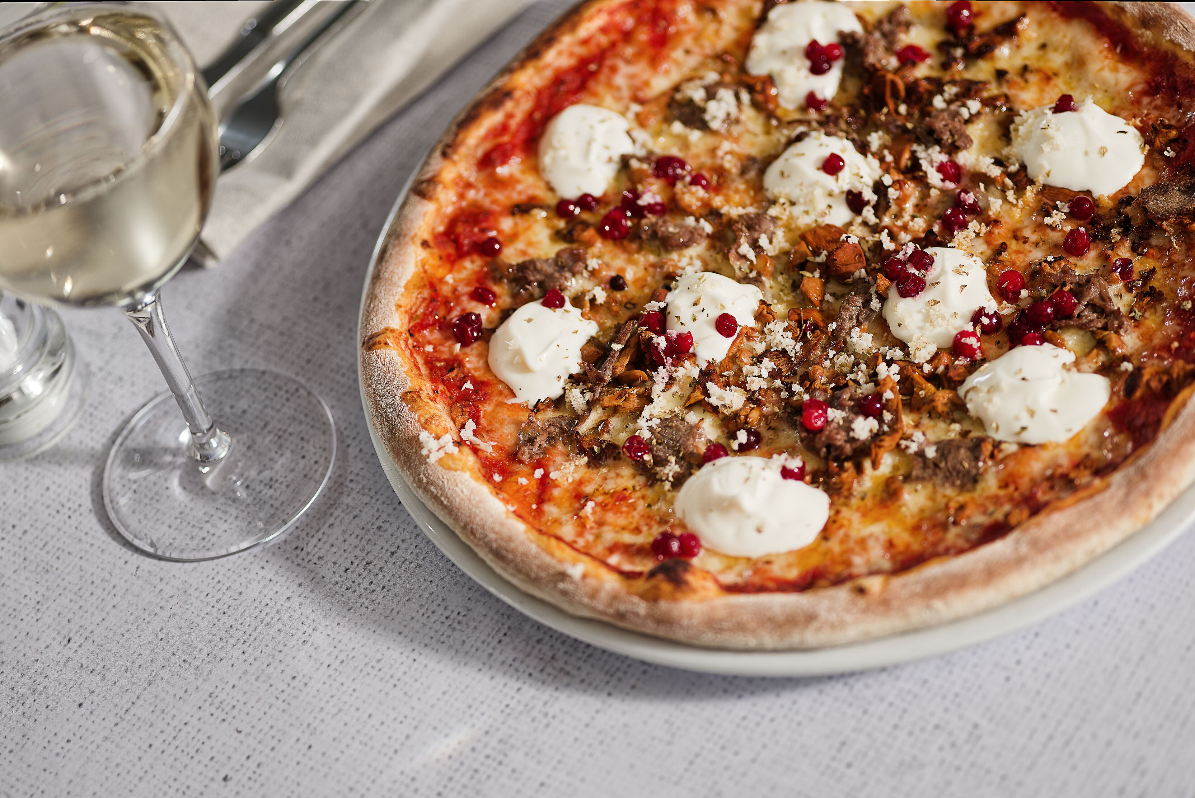 A pizza with toppings and a glass of white wine on a table.