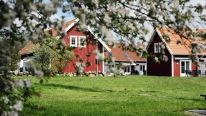 A row of red wooden houses with a grassy lawn in front. - Apelviken Lägenhetshotell (Varberg)