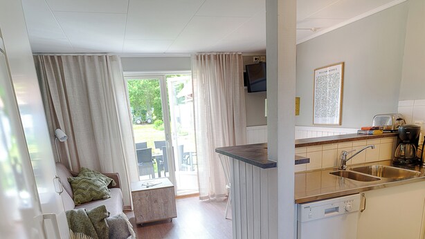 A compact kitchen with a dishwasher, a sink, and a small dining area with a table and chairs. - Apelviken Lägenhetshotell (Varberg)
