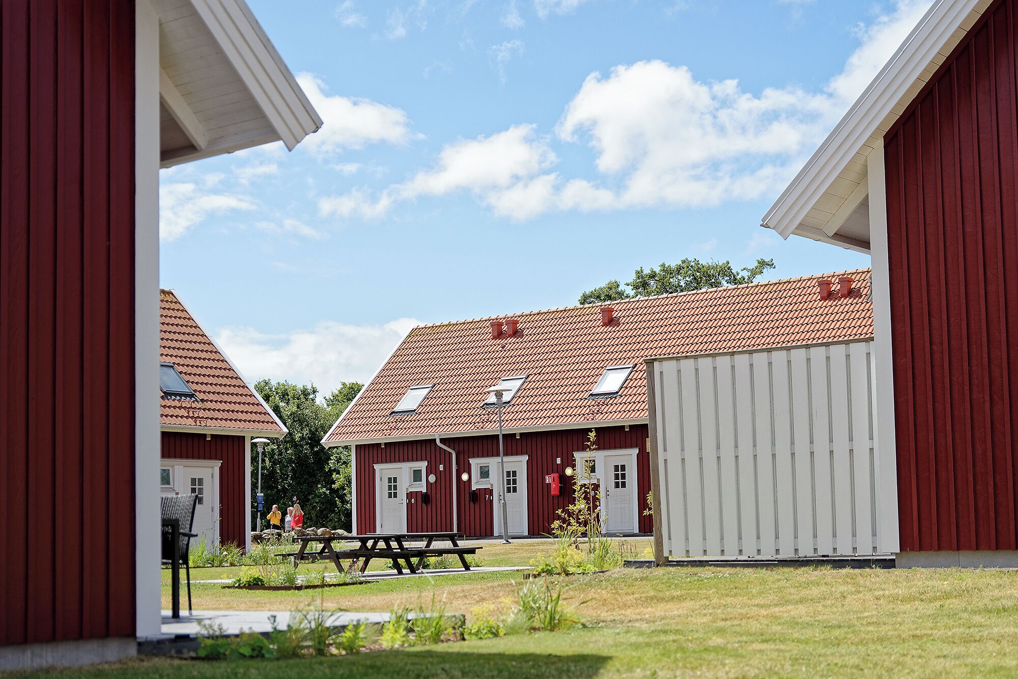 A row of red buildings with white doors, a picnic table, and a clear sky.