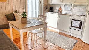 A compact kitchen with white cabinets, a wooden table, and a gray rug. - Apelviken Lägenhetshotell (Varberg)