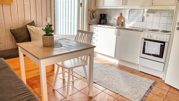 Cocina compacta con armarios blancos, una mesa de madera y un tapete gris.