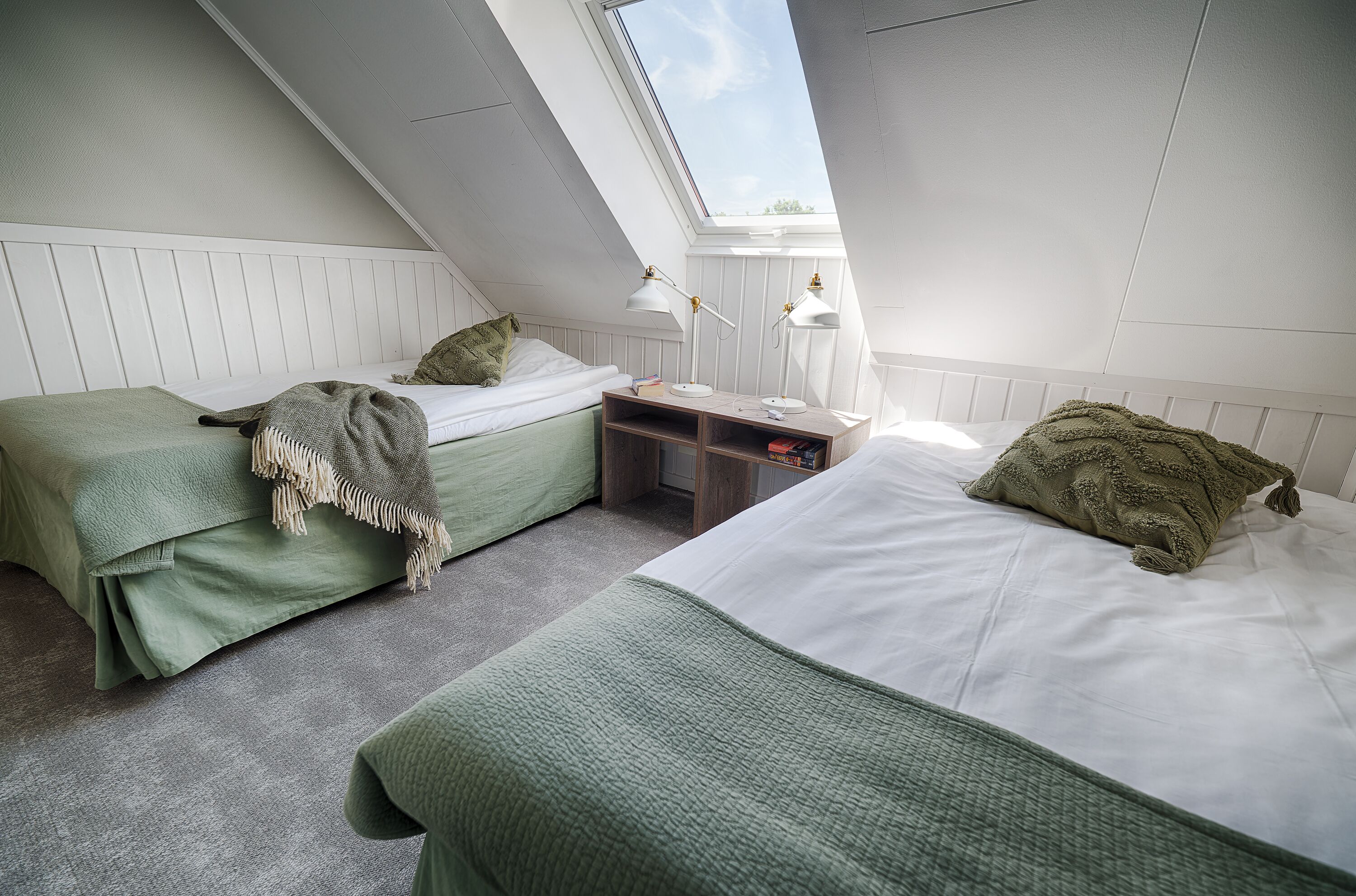A bedroom with two beds, a skylight, and a small desk with lamps.