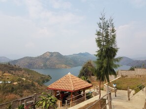 A gazebo with a tiled roof overlooking a lake and hills.