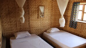 Una habitación con dos camas de madera, ropa de cama blanca, un diseño tejido en la pared, una ventana con cortinas y un dosel blanco colgante.