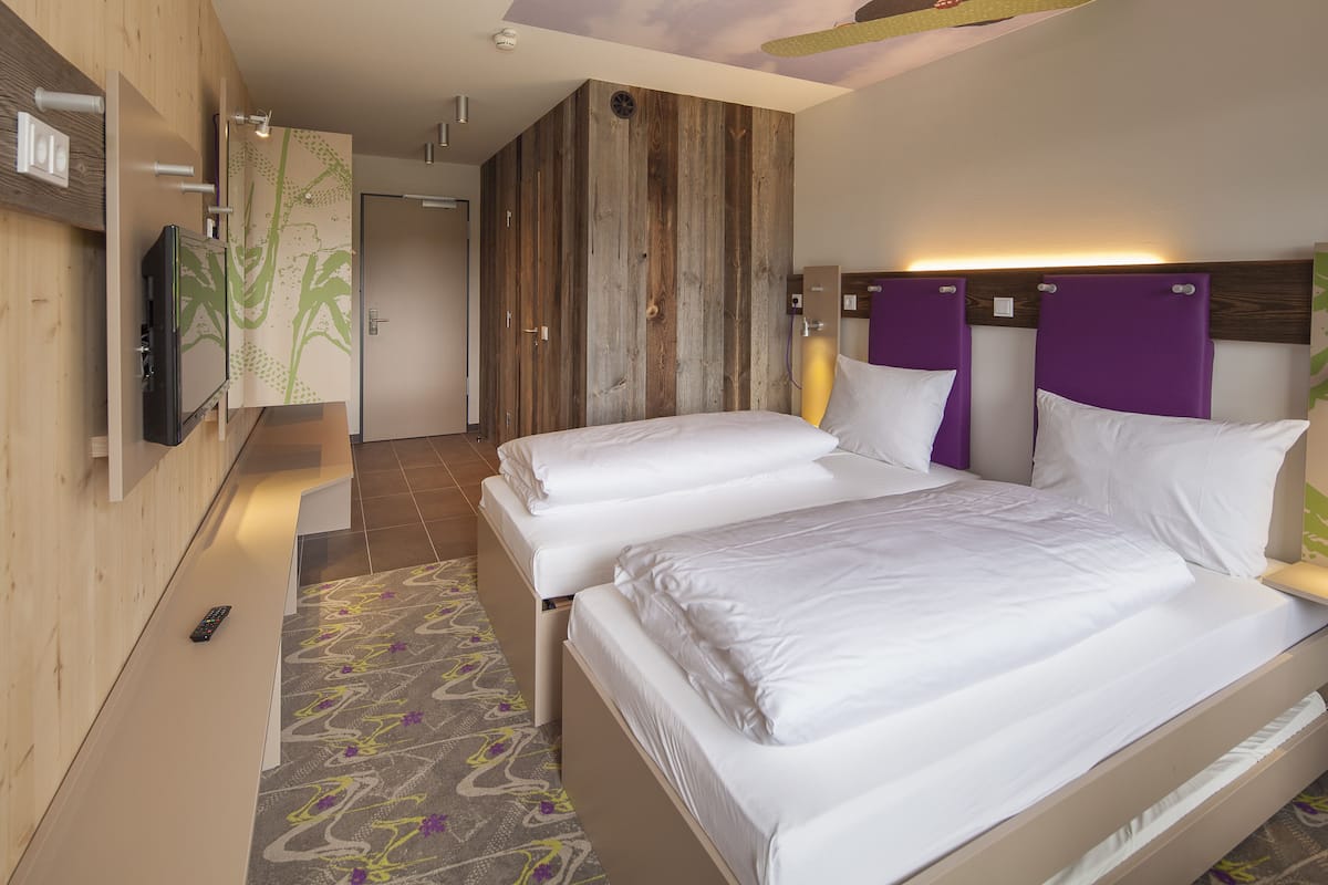 A hotel room with two beds, a television, and a wooden accent wall.