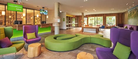Rebuda d'hotel moderna amb una taula de recepció, zones d'estar i una pantalla de televisió que mostra un missatge de benvinguda.