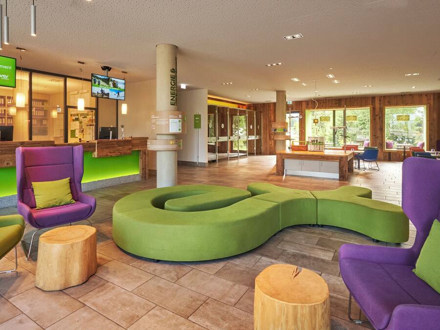 En modern hotellobby med en receptionsdisk, sittgrupper och en tv-skärm som visar ett välkomstmeddelande.
