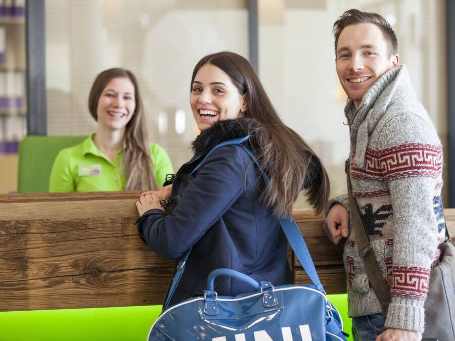 A reception area with wooden reception desk, green seating, and a person in a blue jacket.