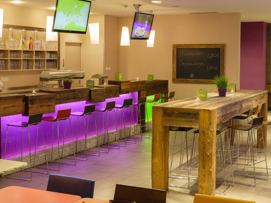 A bar area with a wooden counter, multiple bar stools, and a television screen.