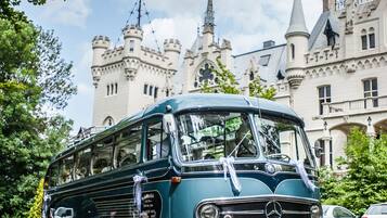 A vintage green bus parked in front of a castle-like building with multiple towers and spires.
