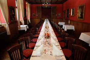 A long dining table set with chairs, a chandelier, and framed portraits on the walls. - Kommende Ramersdorf (Bonn)