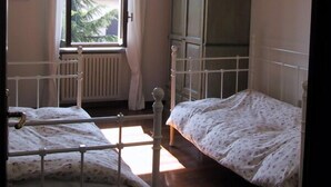 Un dormitori amb dos llits, una finestra amb cortines, un radiador i un armari.