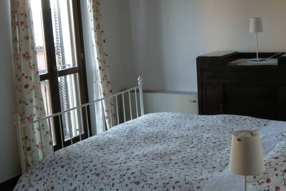 Ein Schlafzimmer mit einem Bett, einem Nachttisch, einer Lampe und einem Fenster mit floralen Vorhängen.