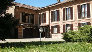 Un edifici de maó de dos pisos amb teulada de rajola, diverses finestres amb persianes i una zona d'entrada pavimentada.