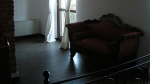 Habitació amb sòl de fusta, un sofà de tons foscos, una finestra amb cortines transparents i una paret de maó.