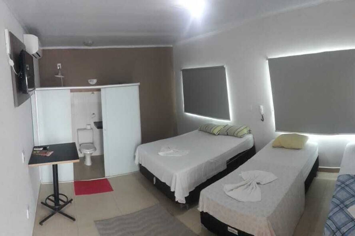 A compact hotel room with two single beds, a small desk, a chair, a TV, and a bathroom.