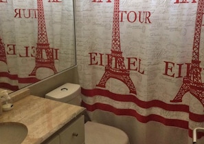 Ein Badezimmer mit Spiegel, Waschbecken und Toilette. Der Duschvorhang zeigt den Eiffelturm und die Silhouette des Wortes 'Eiffel'.