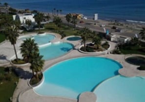 Ein Resort mit mehreren Schwimmbecken, umgeben von Palmen und Blick auf den Ozean.