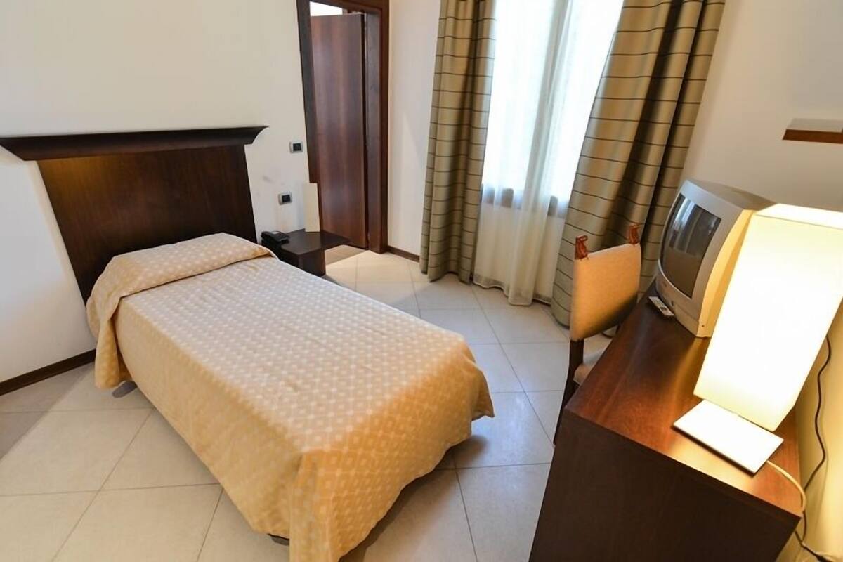 A hotel room with a bed, a desk with a computer, a TV, and a window with curtains.